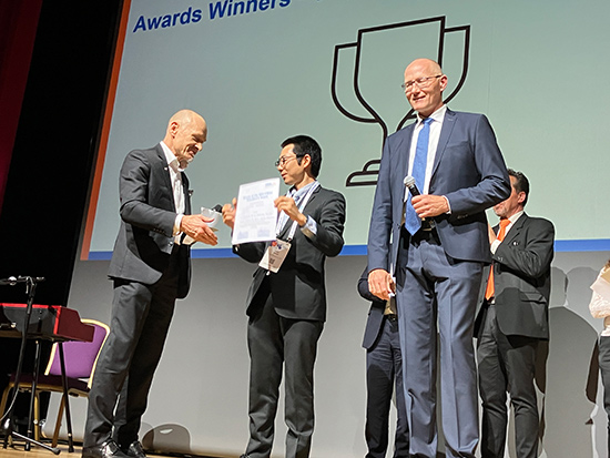 Senior Specialist of IHI Power Systems, Mr. Yutaka Masuda (center), accepts the President’s Award on behalf of IHI Power Systems from former CIMAC President Klaus Heim (left) after a welcome to the stage by CIMAC President Rick Boom (right)